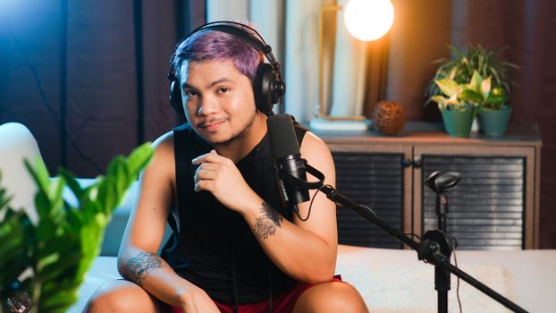 Musician sitting indoors with headphones and microphone, ready to record a podcast.