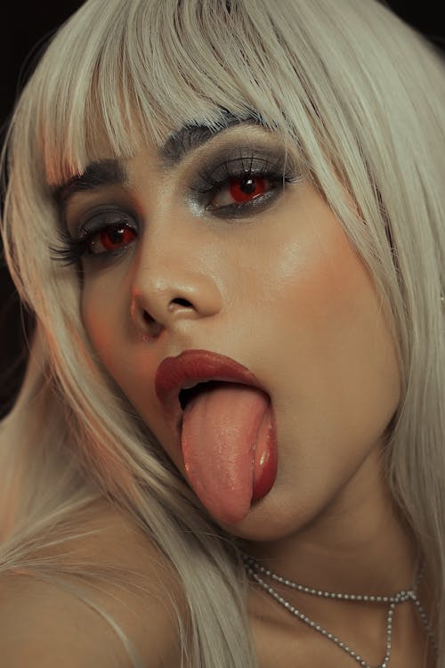 Free A woman with long blonde hair and red eyes sticking out her tongue Stock Photo