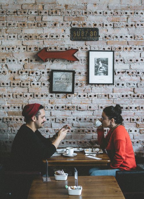 Free Two people enjoying coffee and conversation in a rustic brick-walled café. Stock Photo