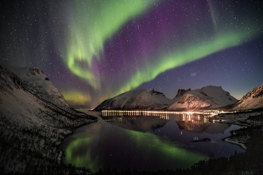 Breathtaking view of the Northern Lights dancing over snowy mountains and a reflective river at night.