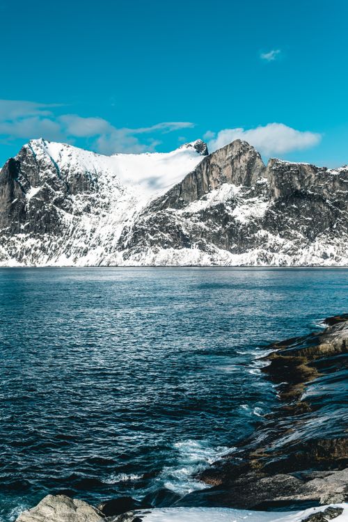 Free Scenic view of snow-capped mountains by a clear blue lake, under a bright winter sky. Stock Photo