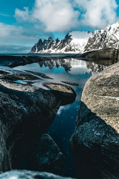 前景是崎岖的岩石，水晶般清澈的湖泊倒映着令人叹为观止的雪山