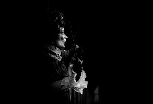 Black and white photo of a Venetian masked performer holding a wand, evoking mystery and drama.