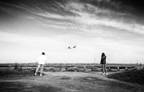 Two people are standing on a dirt road near a plane