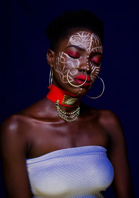 Bold and artistic portrait of a woman with intricate face paint and elegant jewelry against a dark background.
