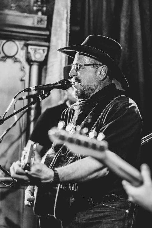 Free Black and white photo of a musician singing and playing guitar on stage. Stock Photo