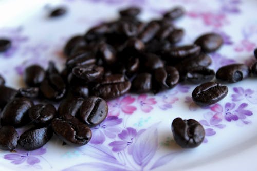 Closeup heap of aromatic roasted coffee beans placed on tablecloth with floral ornament