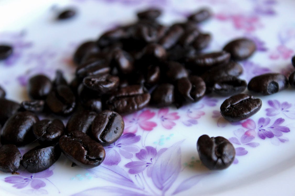 Free Closeup heap of aromatic roasted coffee beans placed on tablecloth with floral ornament Stock Photo