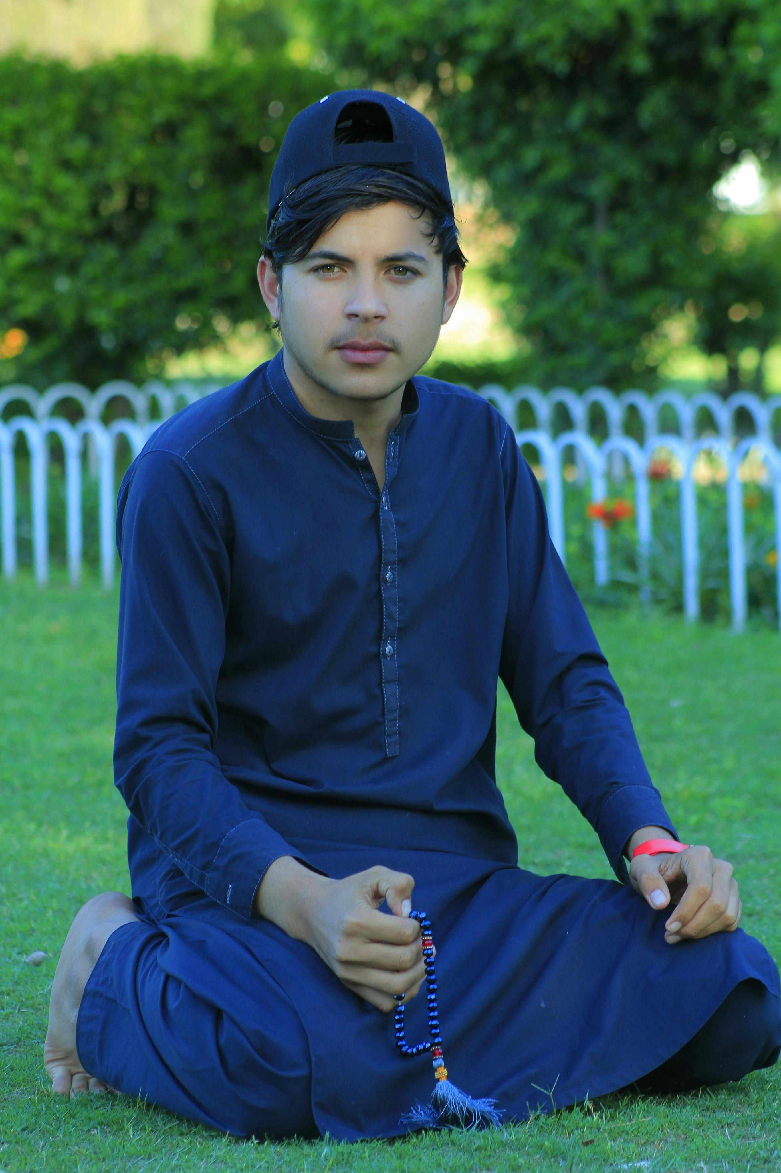 Man kneeling in traditional attire at Yasin Kalan park, holding prayer beads.