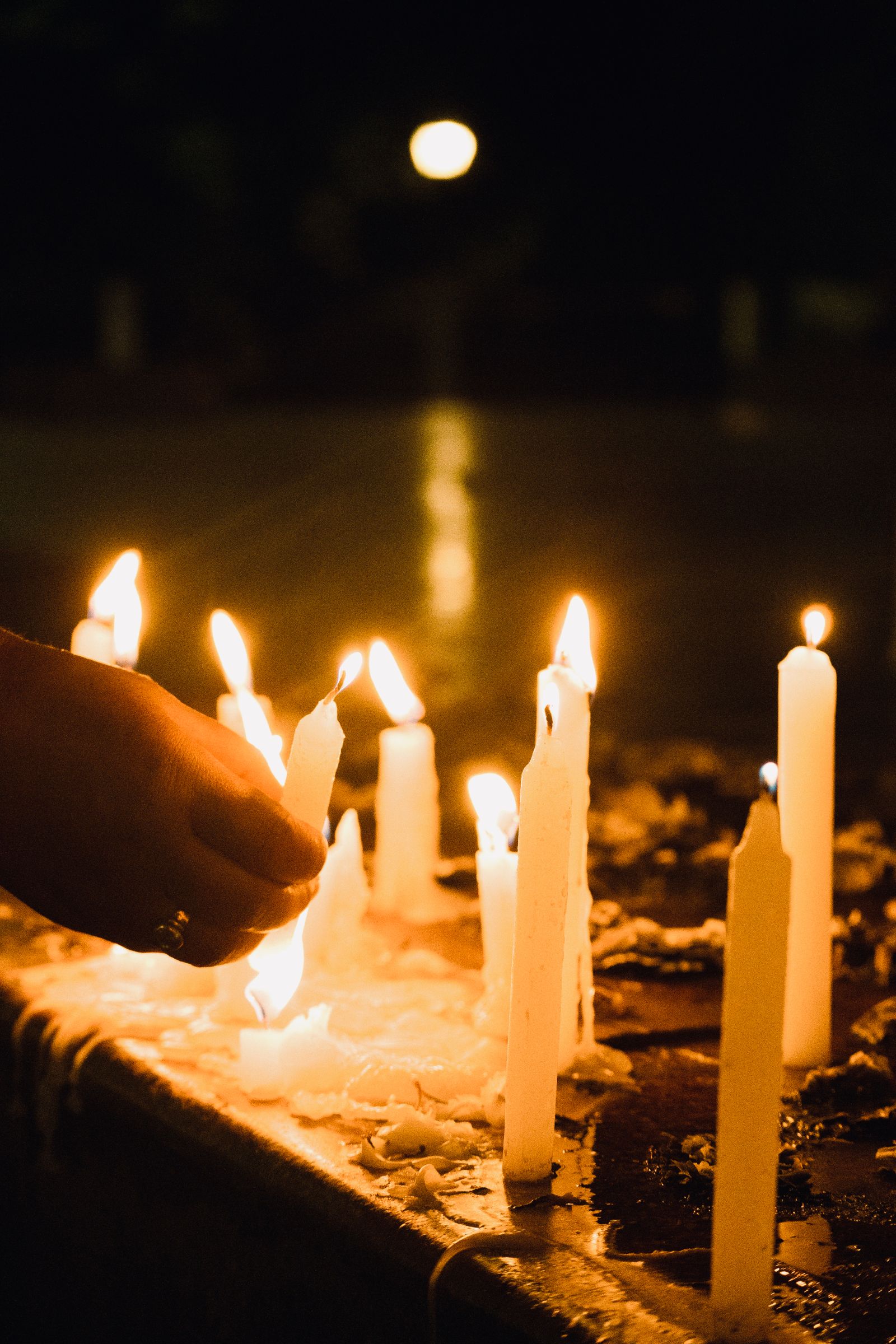 A hand lighting white candles on a stone ledge after dark in Darjeeling, wax pooling around their bases
