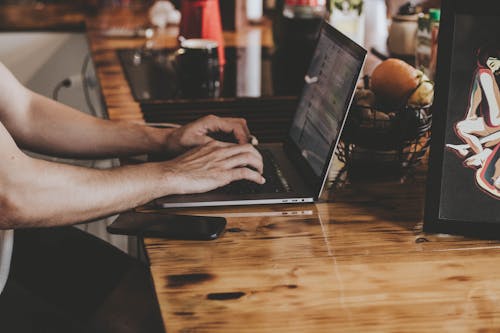 Person In Front Of Laptop On Brown Wooden Table