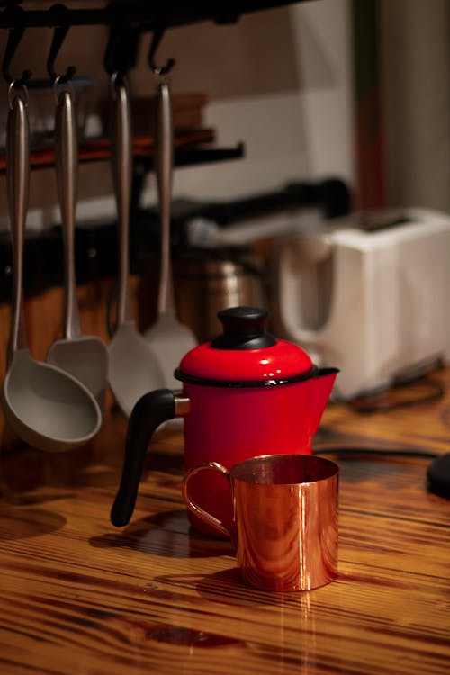 White and Black Kettle Beside Gold-colored Cup on Brown Surface