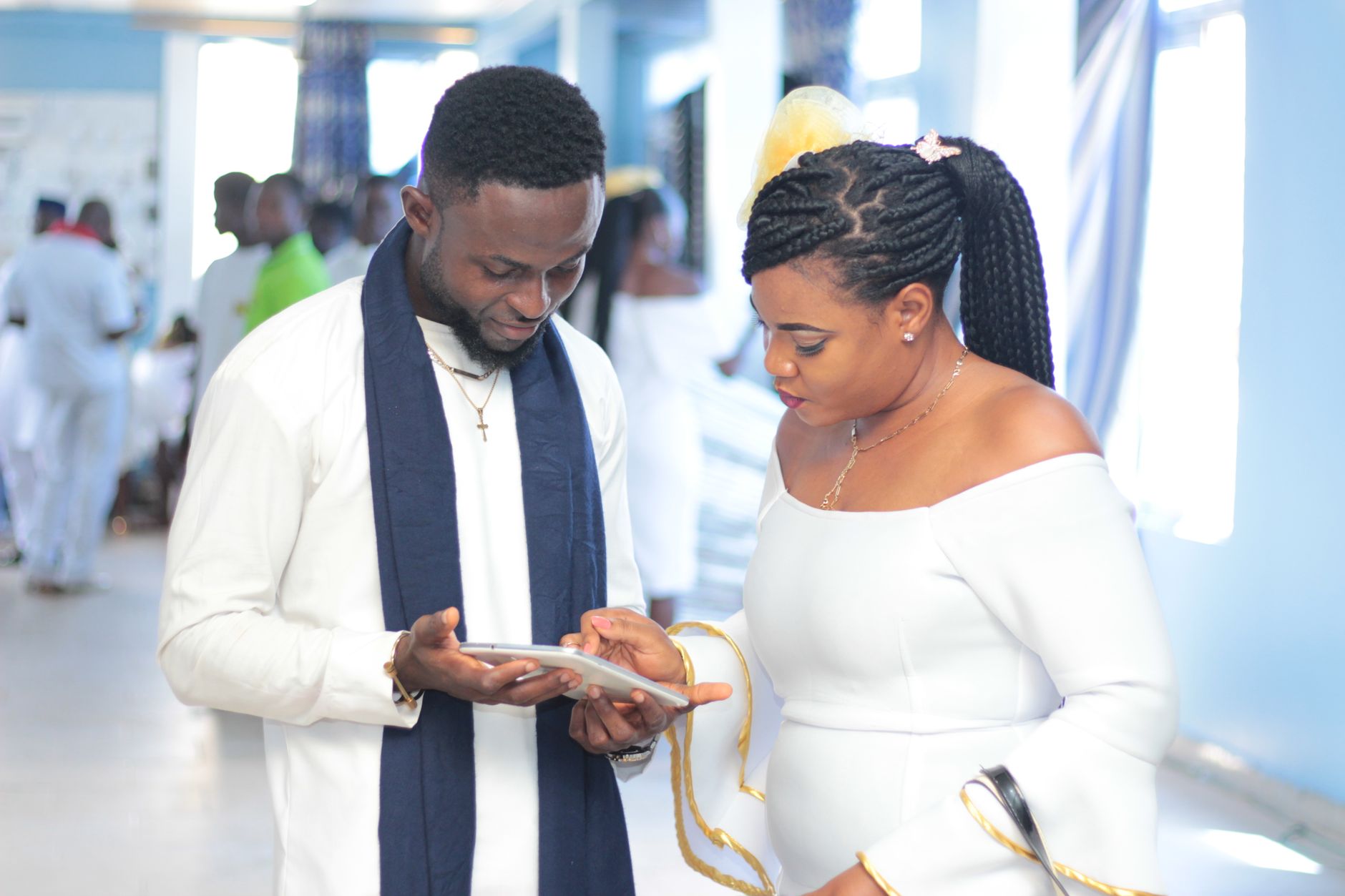 African man and woman engaging with a tablet indoors, dressed elegantly in white.