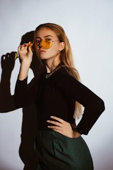 一位时尚的年轻女子在工作室背景下戴着黄色太阳镜摆姿势