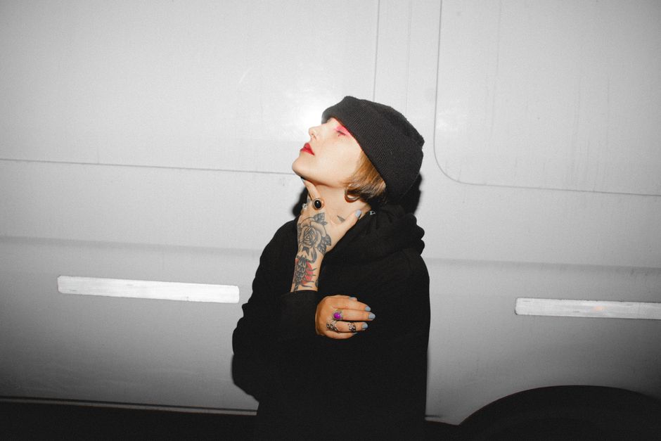 Portrait of a tattooed woman in street style, posing confidently with a stylish beanie against a neutral backdrop.