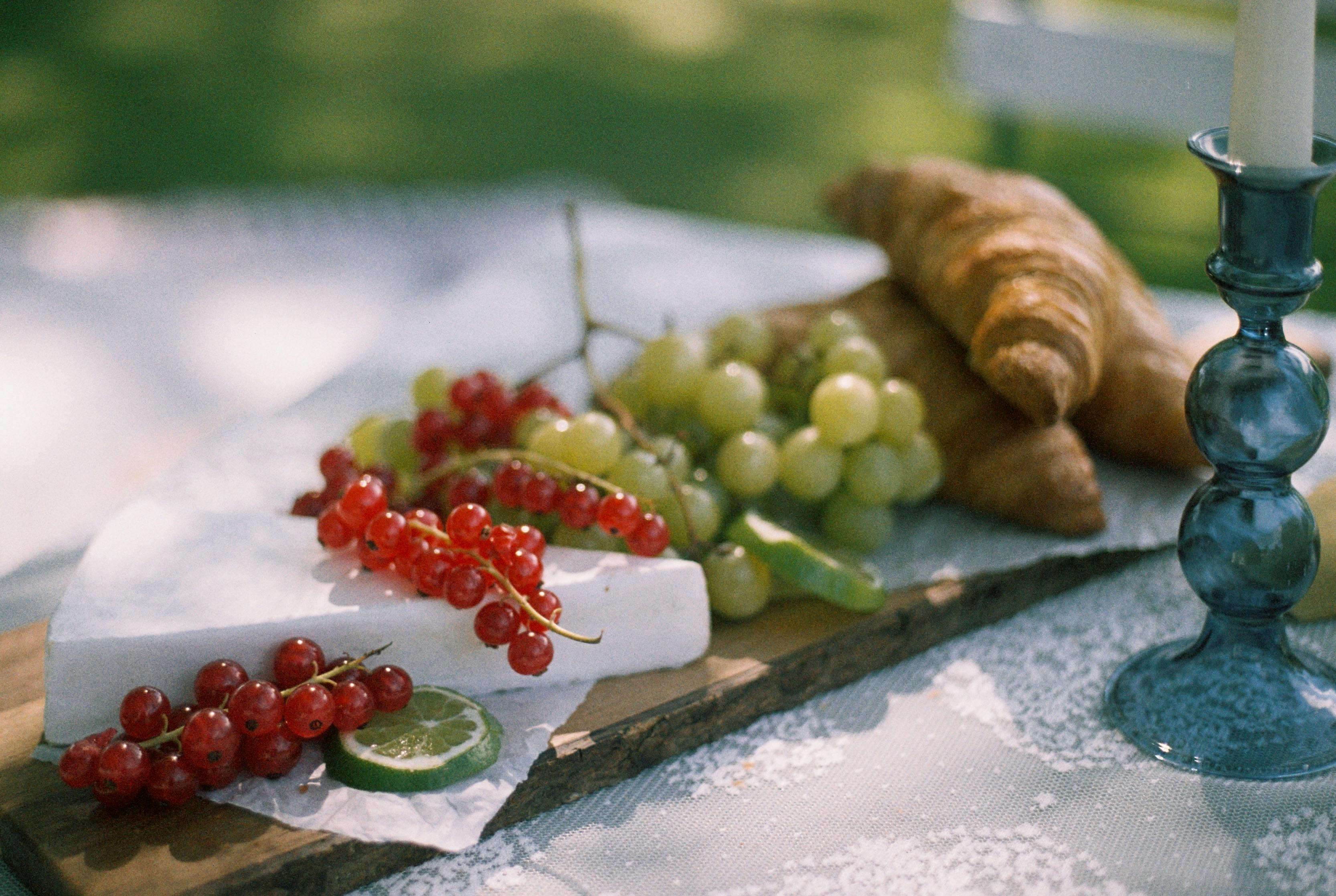 An artistic still life depicting a rustic summer picnic setting in Berlin with croissants, grapes, red currants, and cheese.
