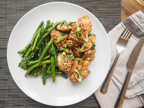 A delicious serving of sesame chicken with fresh green beans on a white plate, perfect for dinner.