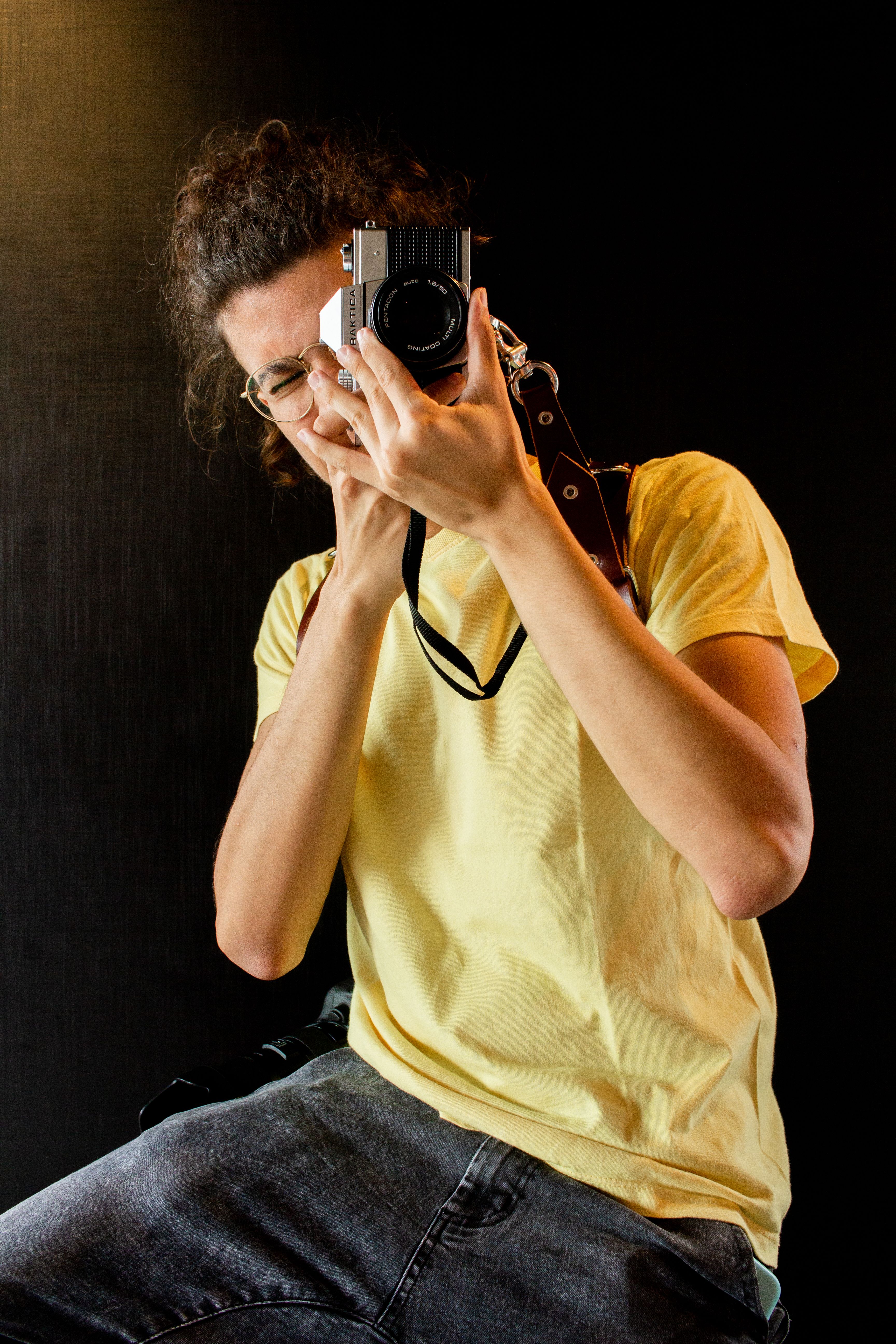 A young adult photographer wearing casual attire captures an image indoors.