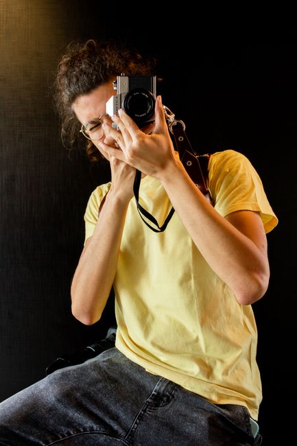 A young adult photographer wearing casual attire captures an image indoors.
