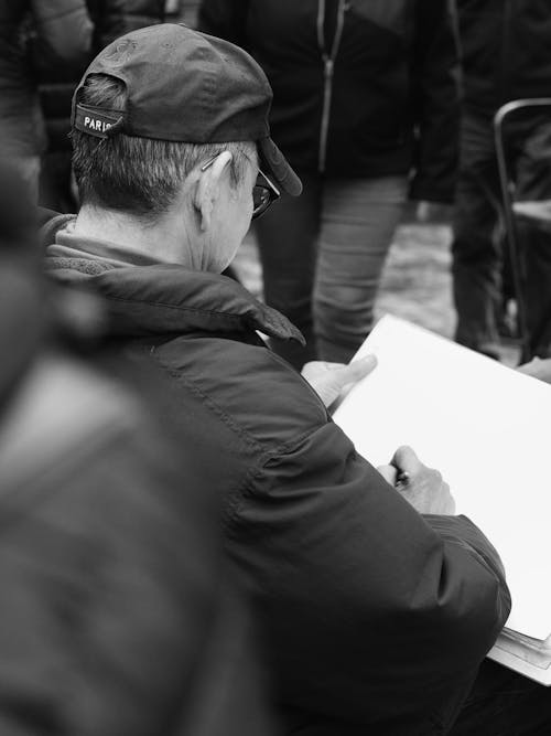 A man in a hat and jacket is writing on a piece of paper