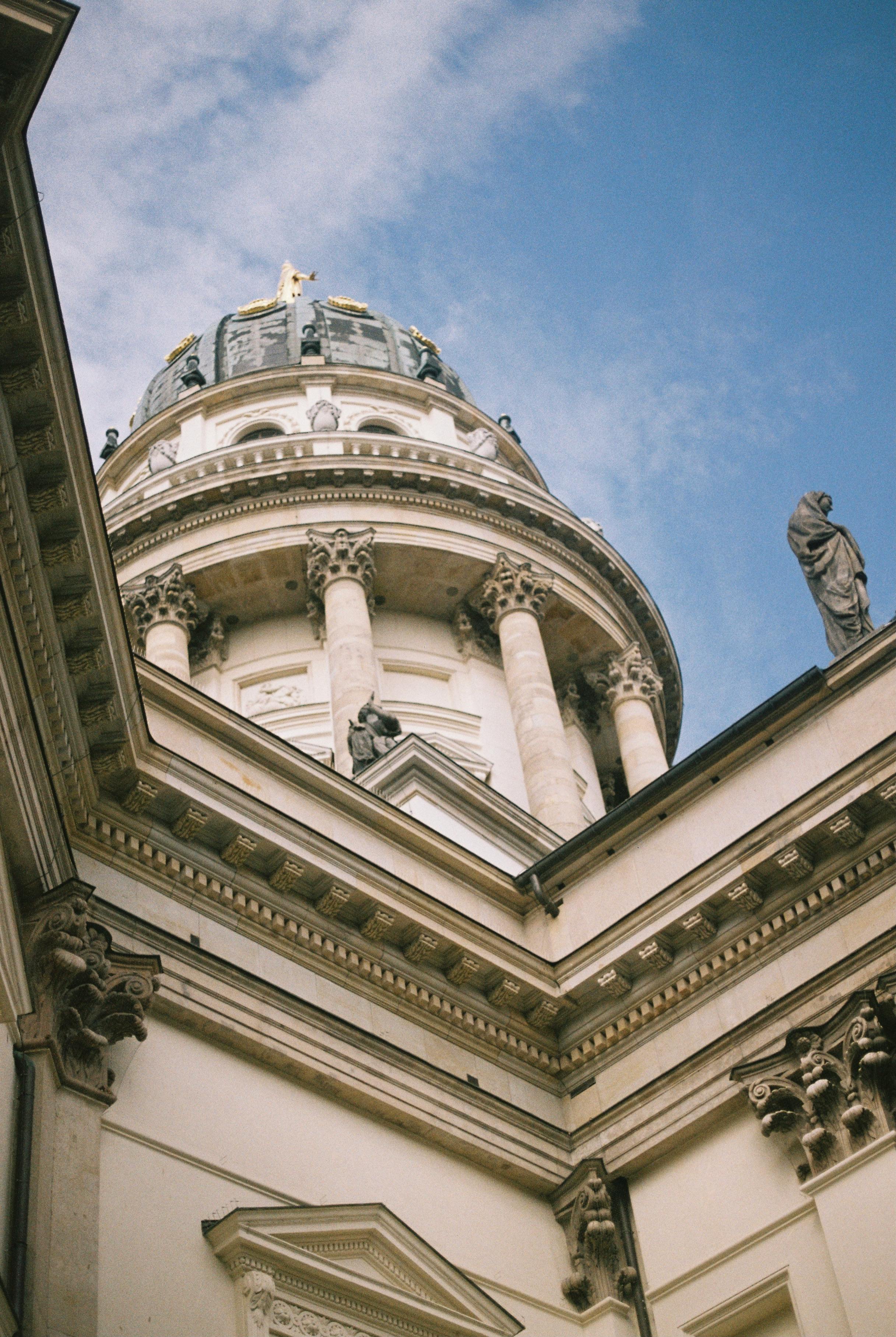Detailed architectural view of French Cathedral in Berlin with blue sky backdrop.