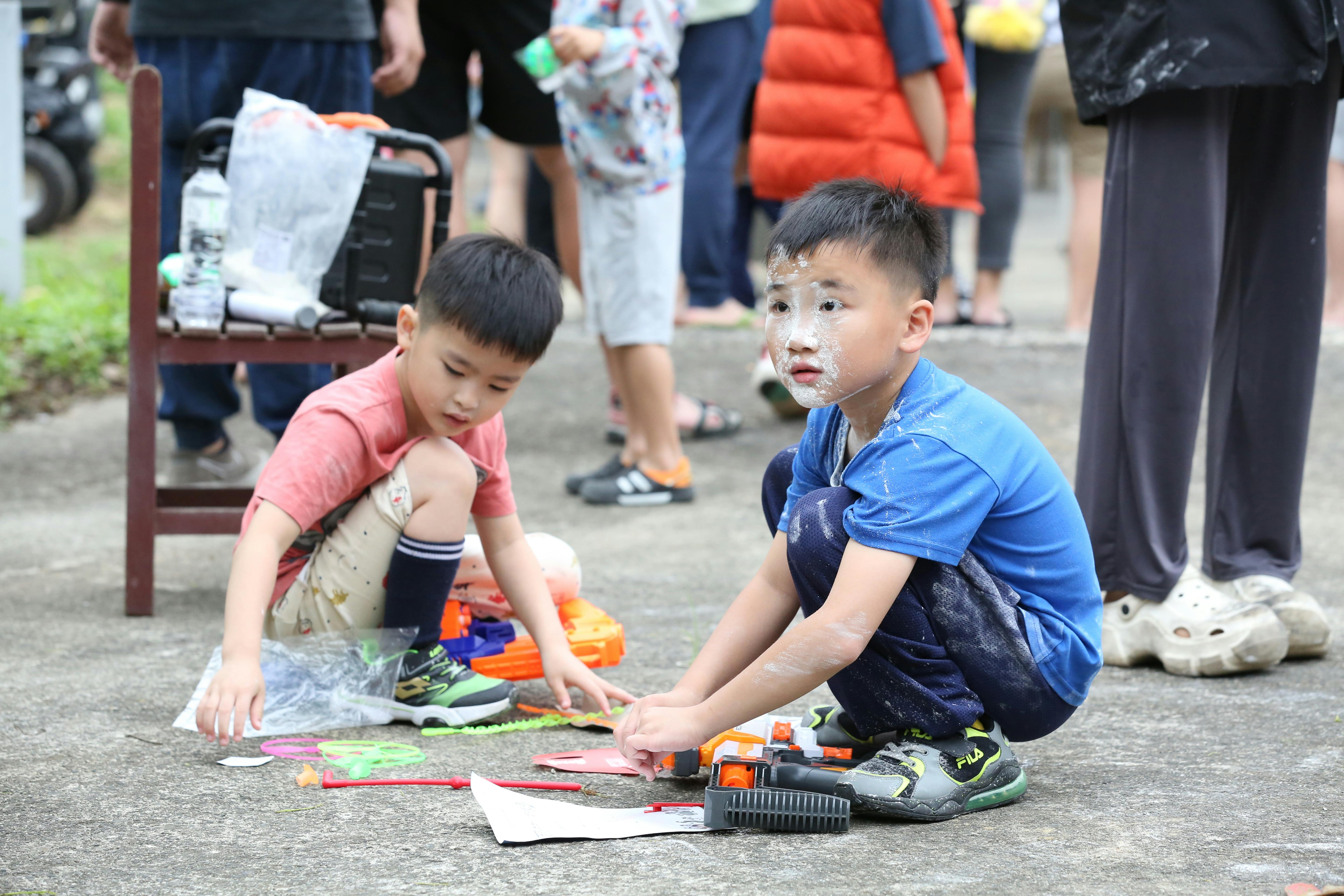 Two boys enjoy playing with toys outdoors at a lively festival gathering.