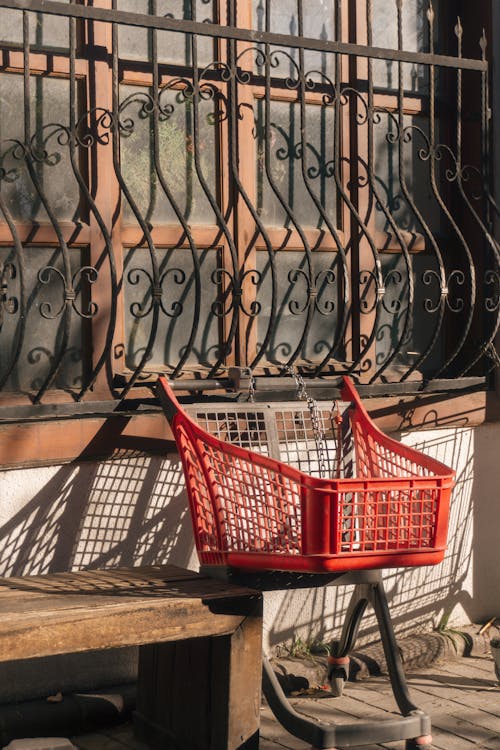 A red shopping cart sitting on a bench outside