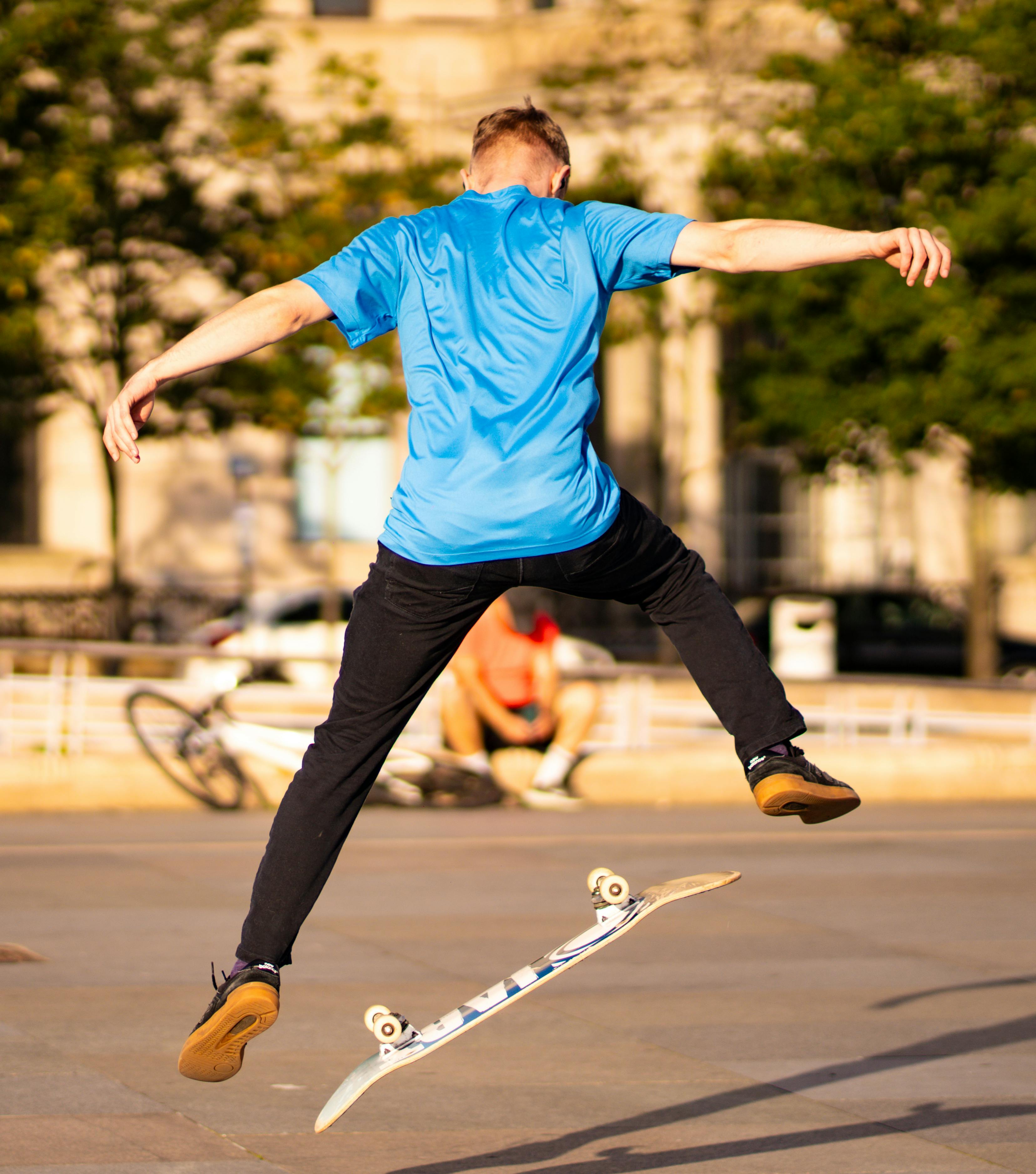 Skater in a blue shirt executes an impressive jump trick at a skatepark during daytime.
