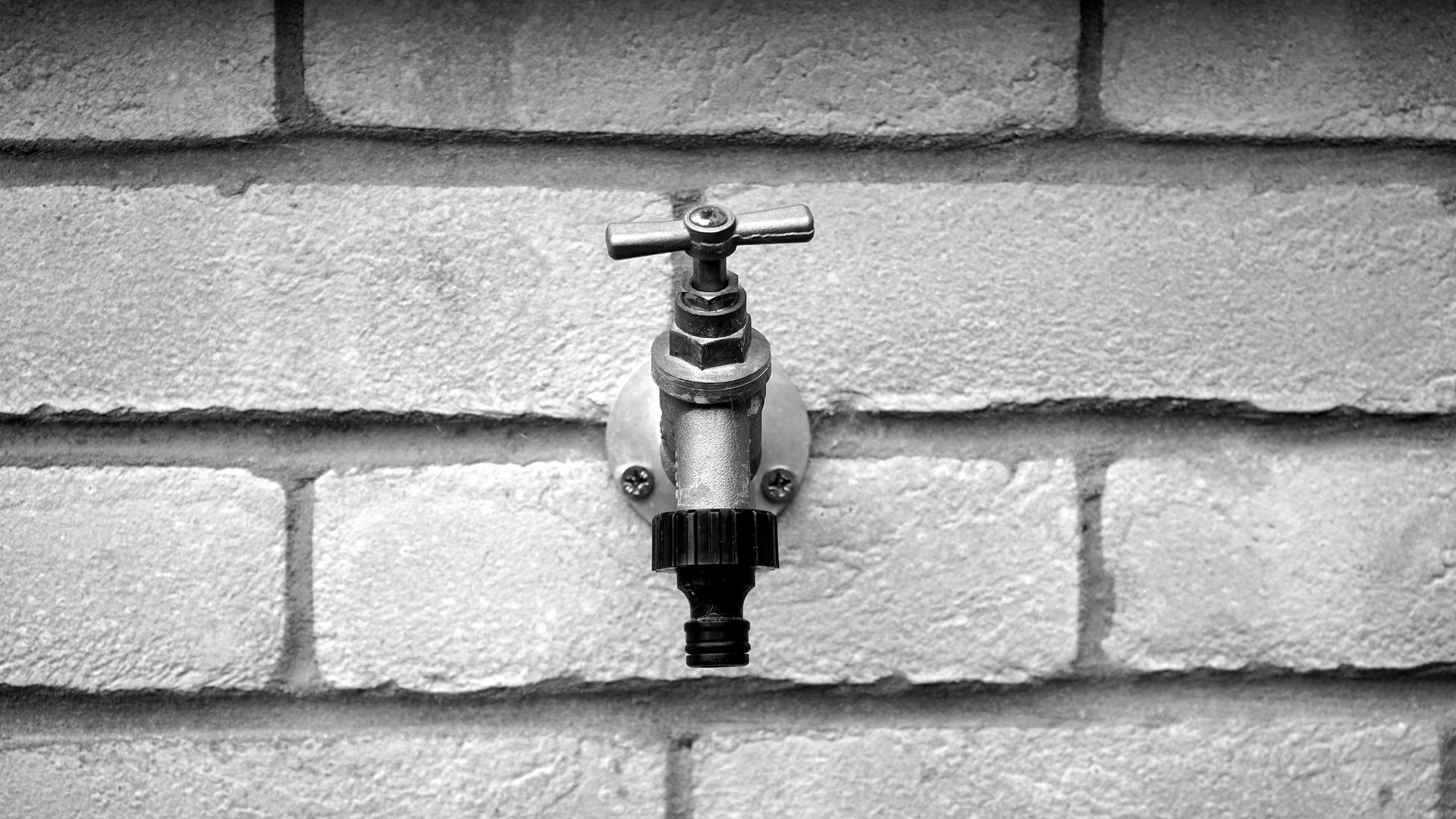 Grayscale of Metal Faucet on Wall Brick