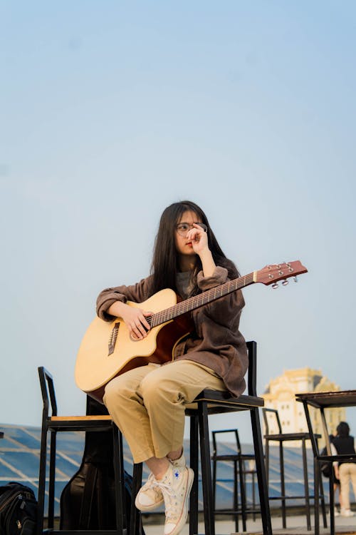 Woman Holding Guitar While Sitting