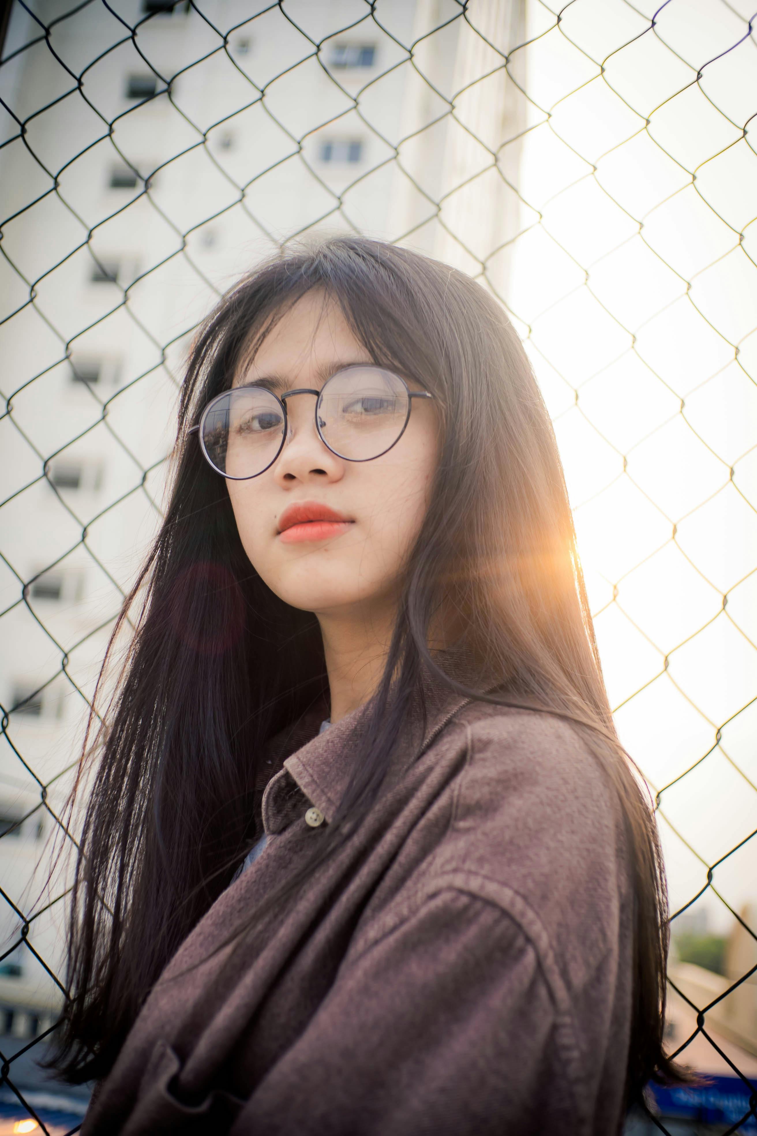 photo of woman in glasses standing by chain link fence