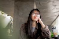 一位戴着眼镜的年轻女子，在室内沉思着喝饮料