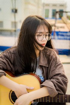 一个戴着眼镜的年轻亚洲女子在阳光明媚的日子里拿着吉他在户外