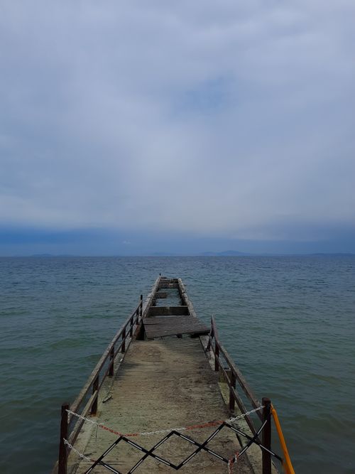 Free A desolate pier stretches into a calm ocean under a cloudy sky, evoking solitude. Stock Photo