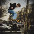 在都市街道的背景映衬下，一名穿着休闲服的滑板者正在表演一个技巧