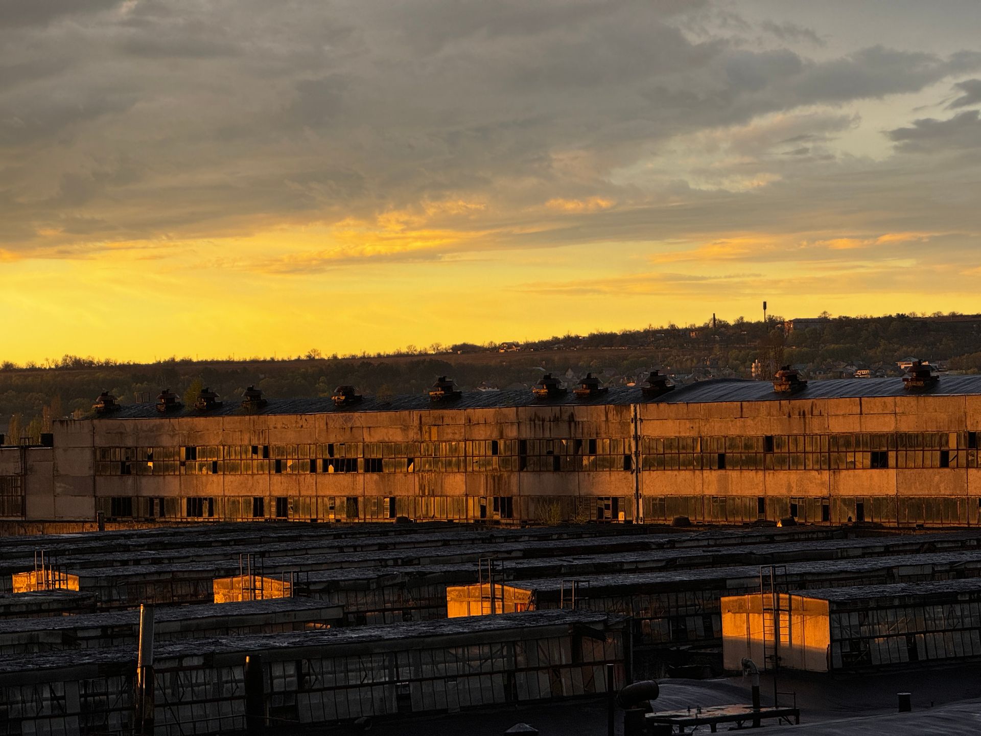 Factory building glowing under a dramatic sunset sky, with scenic golden clouds.
