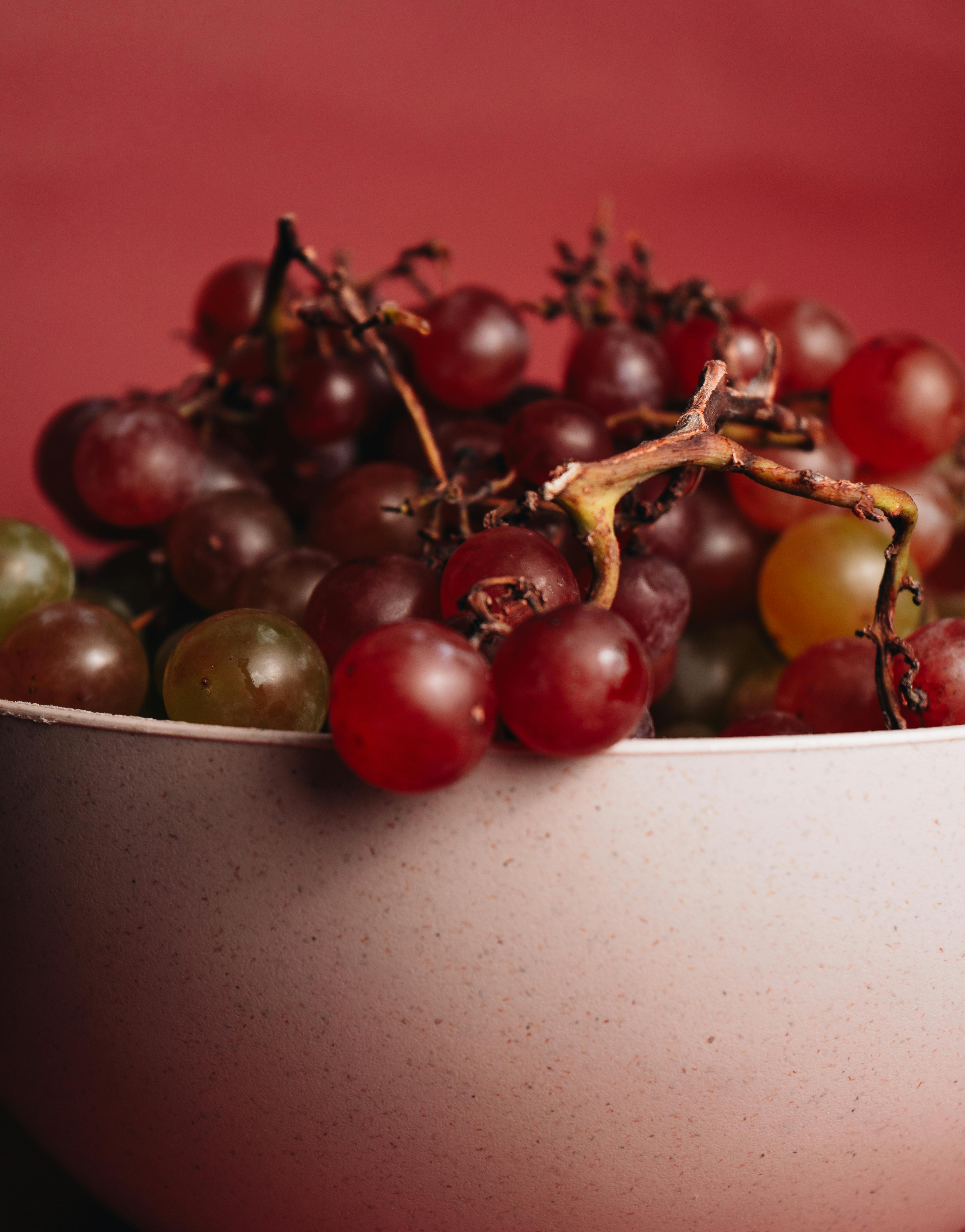 Close-up photo of assorted grapes in a bowl against a red background, perfect for food photography needs.