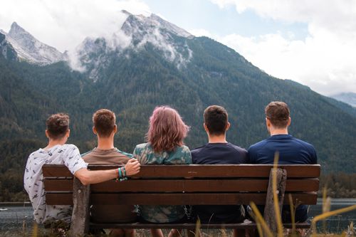 Free Five friends sit together on a bench, taking in the serene mountain view at Hintersee, Austria. Stock Photo