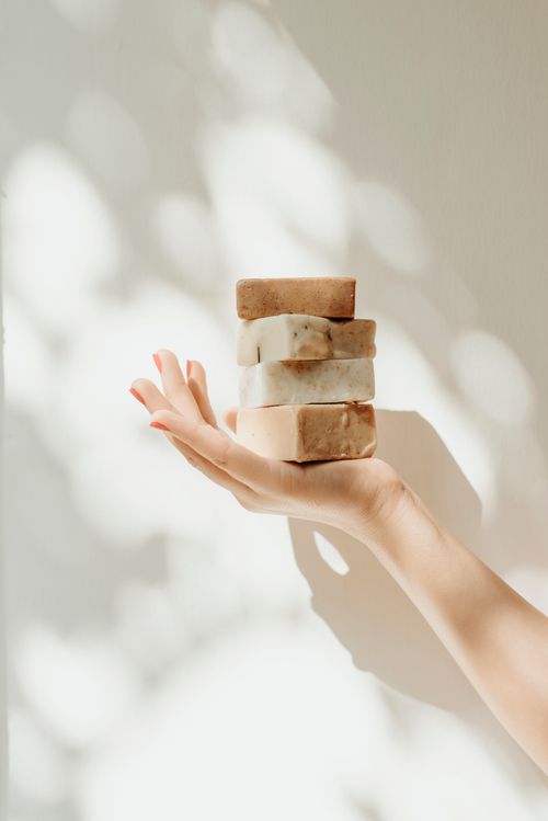 Free A hand holds a stack of artisanal soap bars against a sunlit white background, depicting natural skincare. Stock Photo