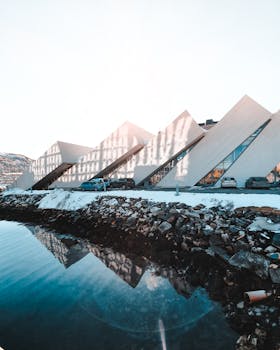 平静的水边倒映着现代几何建筑，背景是冬季