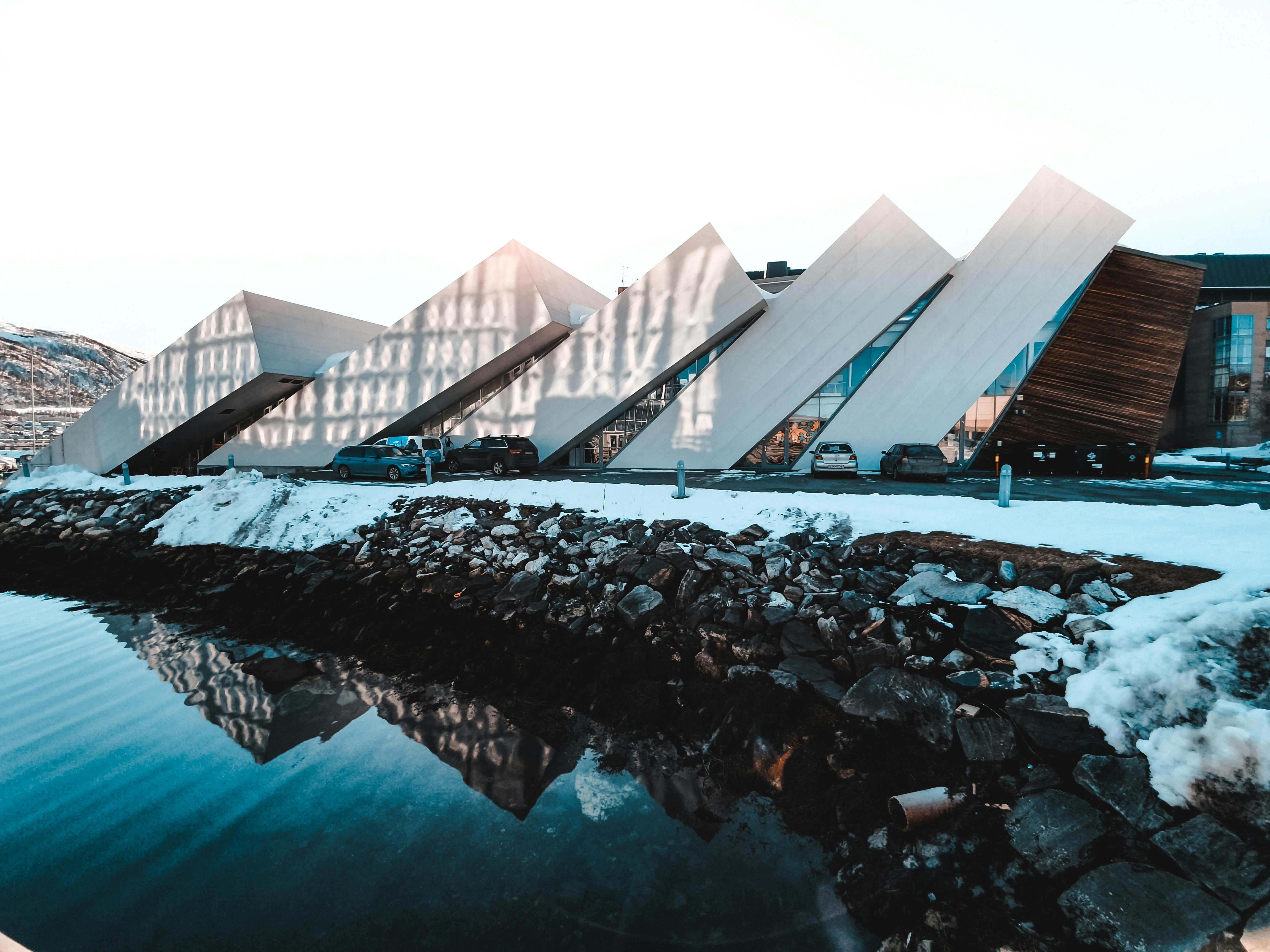 A striking modern building with angular design, reflecting in the water amidst snow.