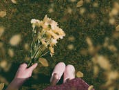 在一个晴朗的日子里，一位女士手捧一束黄花站在草地上