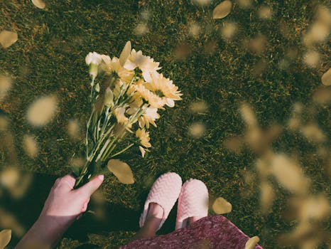 在一个晴朗的日子里，一位女士手捧一束黄花站在草地上