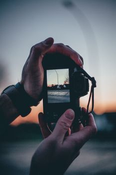 Close-up of hands holding a camera capturing a scenic sunset view.