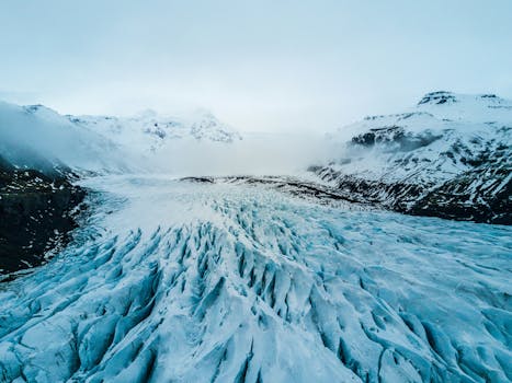 A breathtaking aerial shot of a vast icy glacier surrounded by snow-capped mountains in winter.