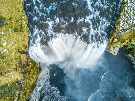 Stunning aerial shot of a powerful waterfall surrounded by rocky terrain and lush greenery.