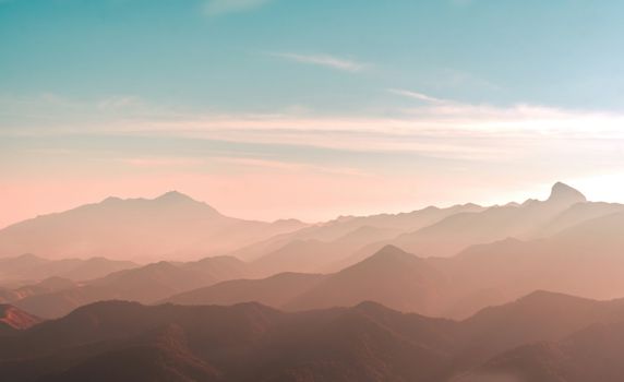 Captivating view of mountains at sunrise with mist and soft hues.