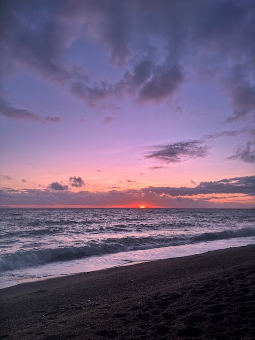 A sunset on the beach with waves and clouds