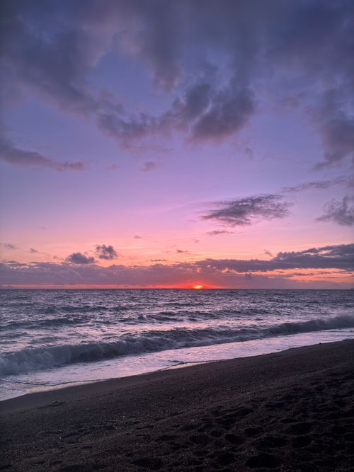 Free Majestic view of the sun setting over a tranquil beach with vibrant hues in the sky. Stock Photo