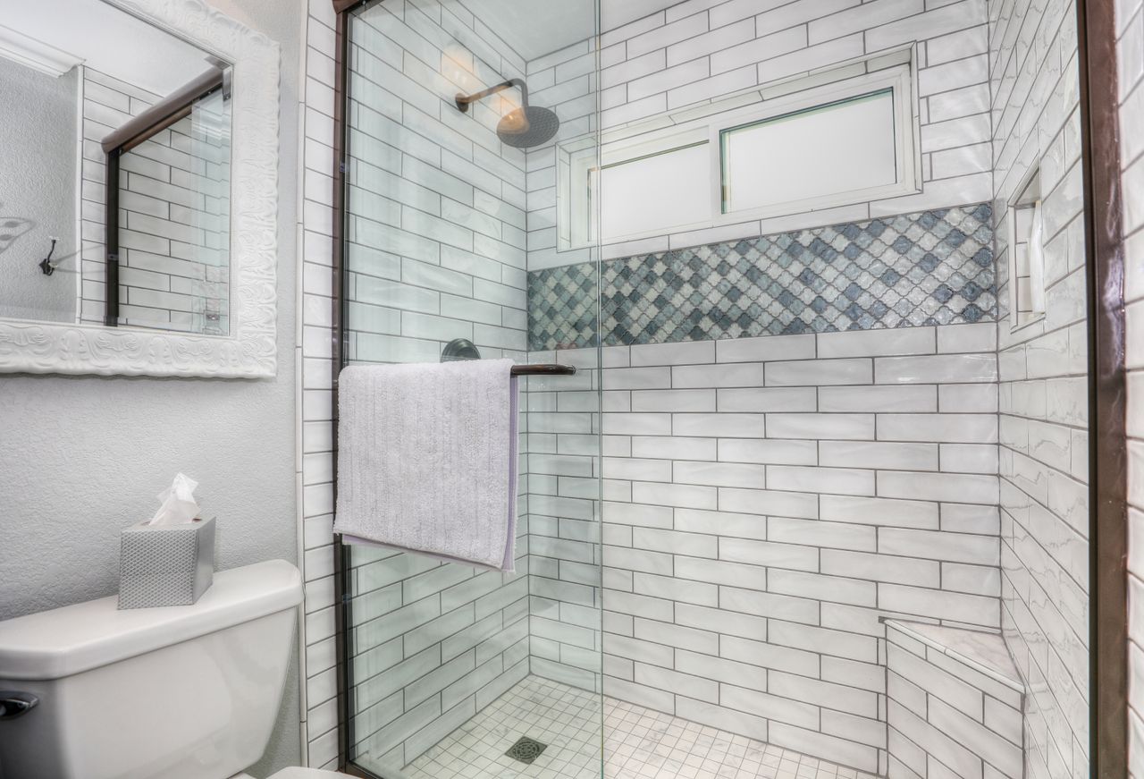 A white subway-tiled shower with bronze-framed glass doors, a mosaic accent band and a small window